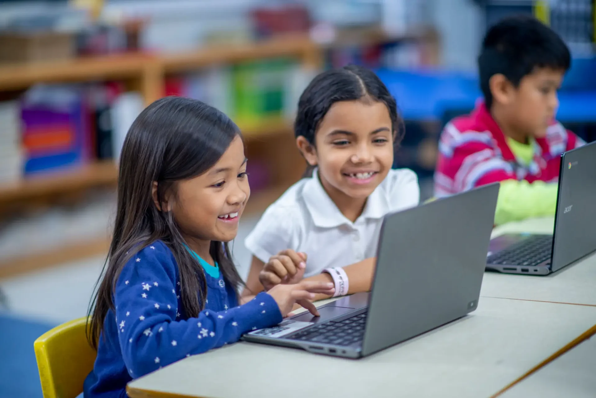 Two girls happily using a laptop together.