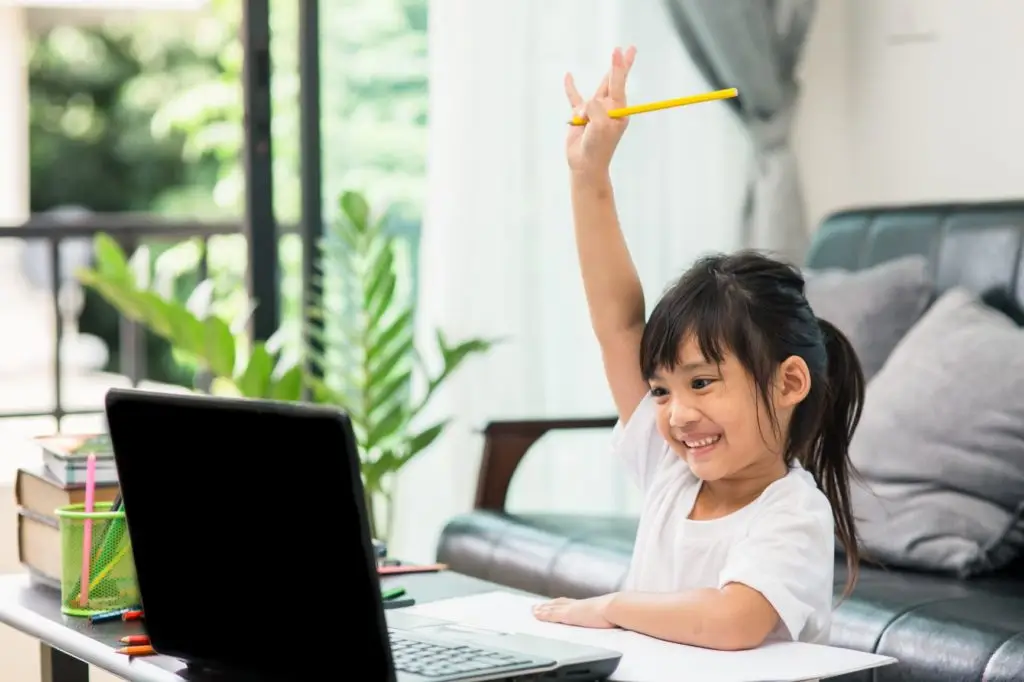 Happy young girl raising hand while learning online at home.